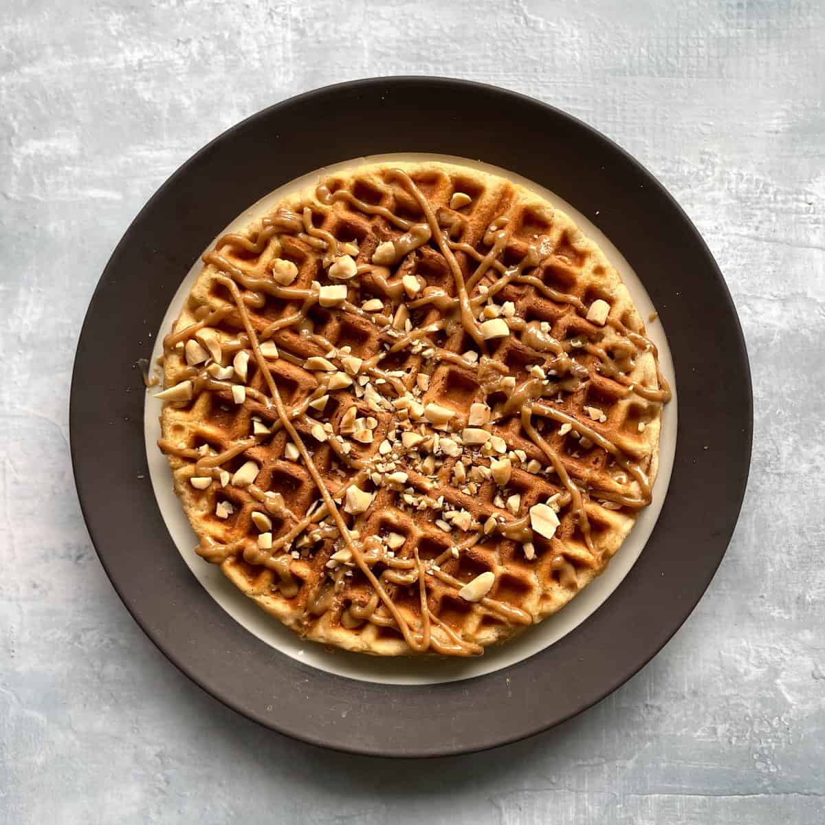 peanut butter waffle on a plate with peanut butter syrup and chopped peanuts.