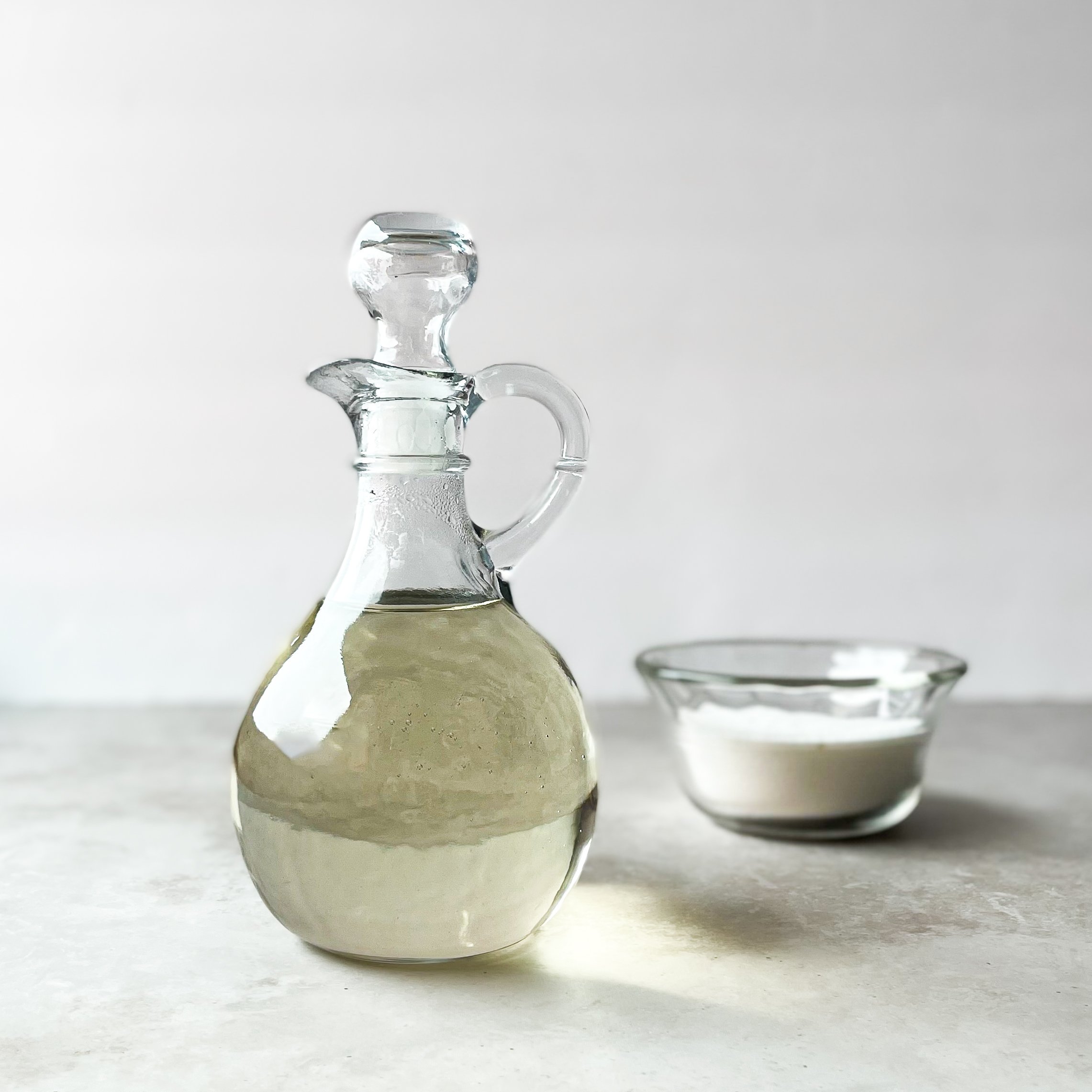 glass jar of simple syrup next to small bowl of sugar. 