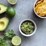 a bowl of four ingredient guacamole, chips, avocados, limes, and cilantro.