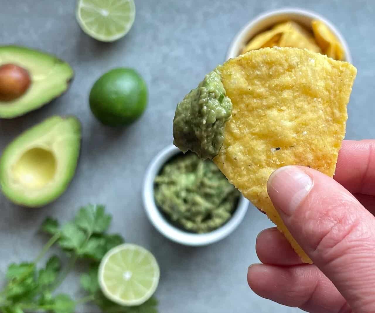 a chip with guacamole and the four ingredients in the background.