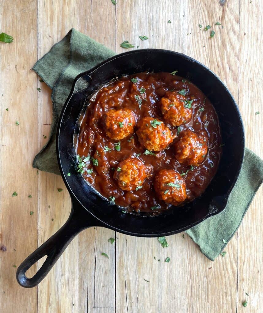 a cast iron pan filled with chicken meatballs and barbecue sauce.