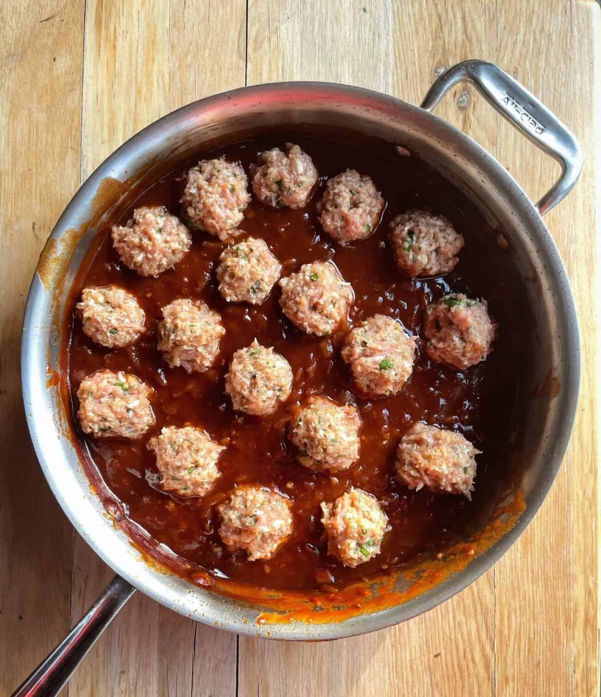 uncooked chicken meatballs sitting in barbecue sauce.