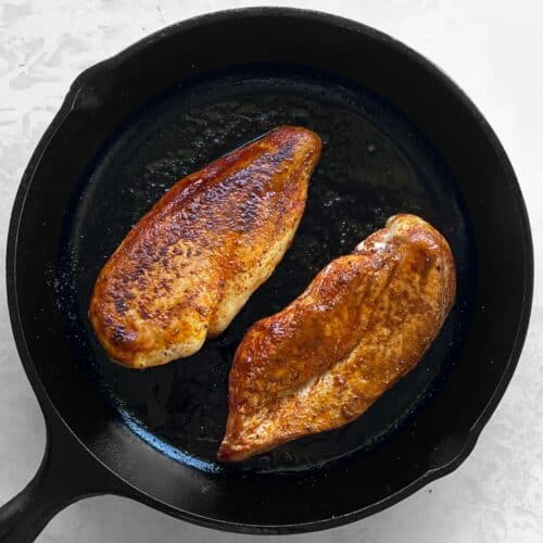 two cooked chicken breasts in a cast iron pan.