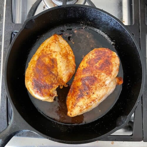two cooked chicken breasts in a cast iron skillet.
