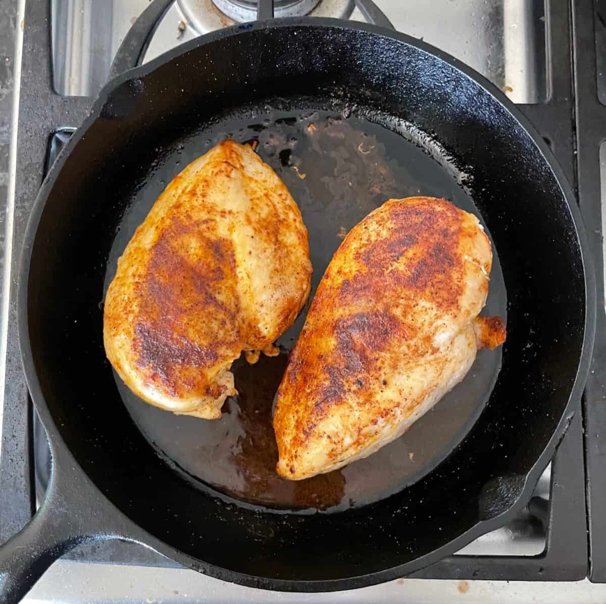 two cooked chicken breasts in a cast iron skillet.