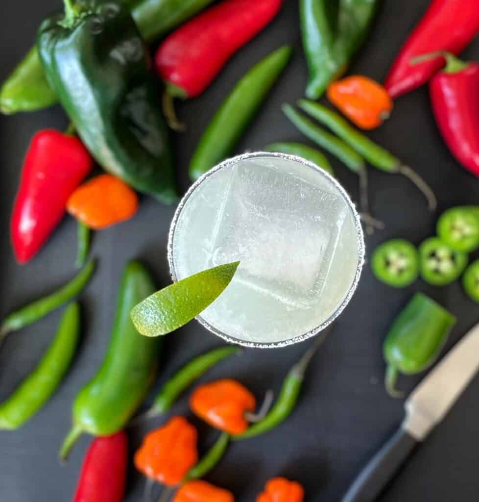 a spicy margarita garnished with lime and surrounded by chili peppers.