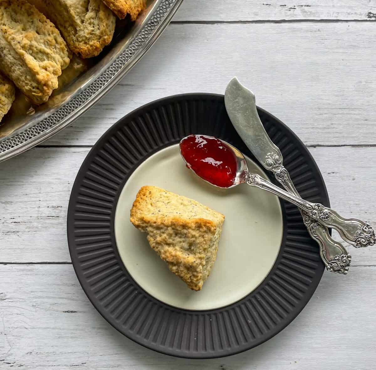 earl grey scone on a plate with knife and spoon with red jam.