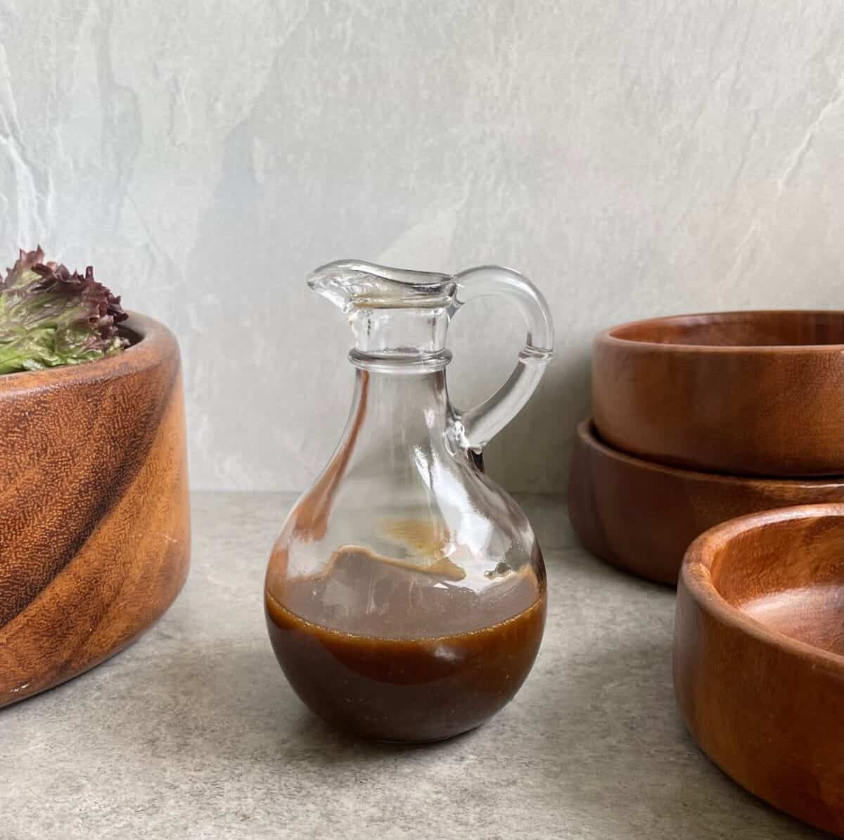a glass carafe of deep brown salad dressing with wood salad bowls.