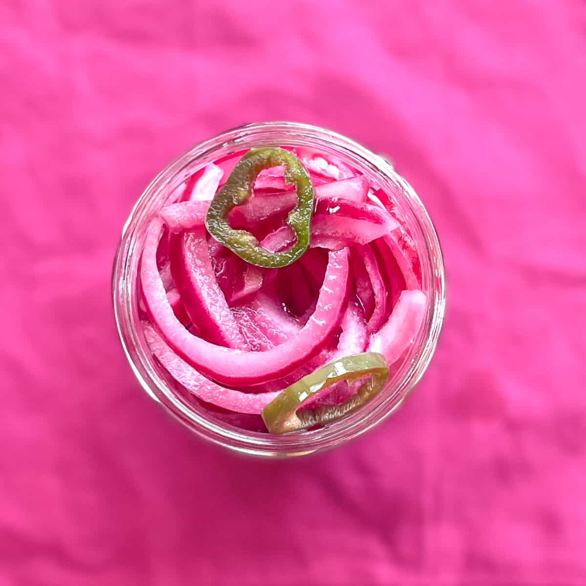 a glass jar of spicy pickled onions with sliced jalapeno peppers.