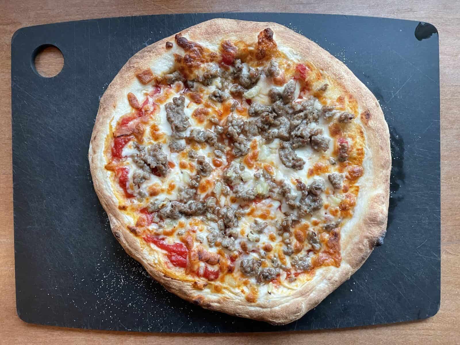 an Ooni sausage pizza on a cutting board.