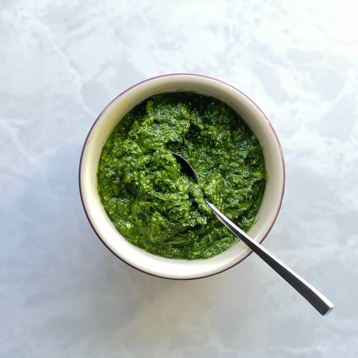 bowl of green pistachio pesto with a spoon.