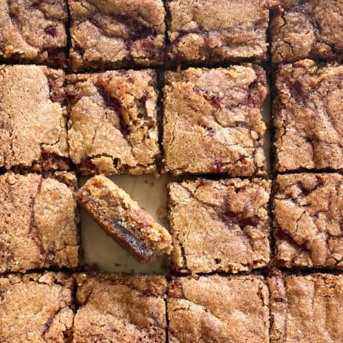 sixteen cut blondies swirled with red jam with one on its side showing the swirled interior.
