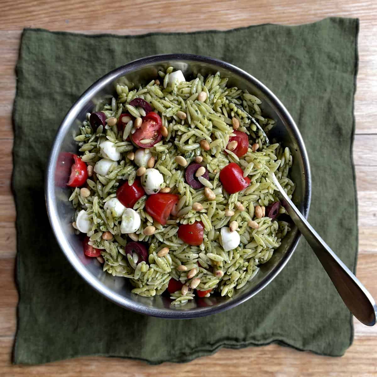 a bowl of green orzo with chopped tomatoes and olives, mozzarella, and pine nuts.