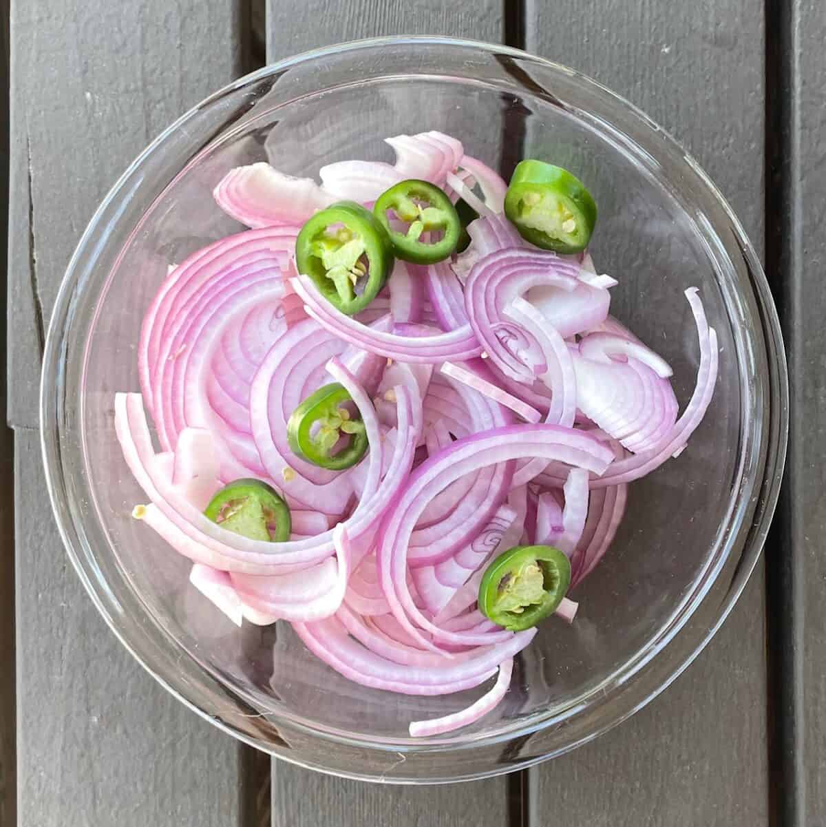 sliced red onion and jalapeno in a glass bowl.