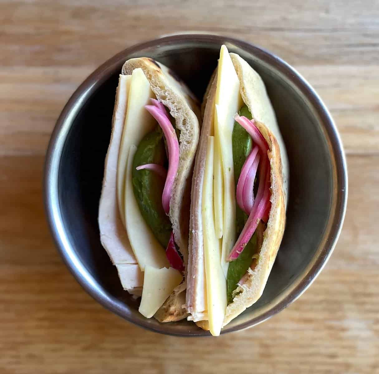 two pita stuffed with turkey, cheese, avocado, and pickled onions.