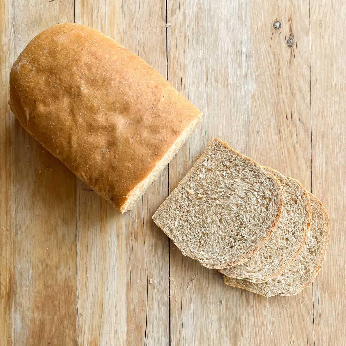 loaf of honey wheat bread and slices on a wood surface.