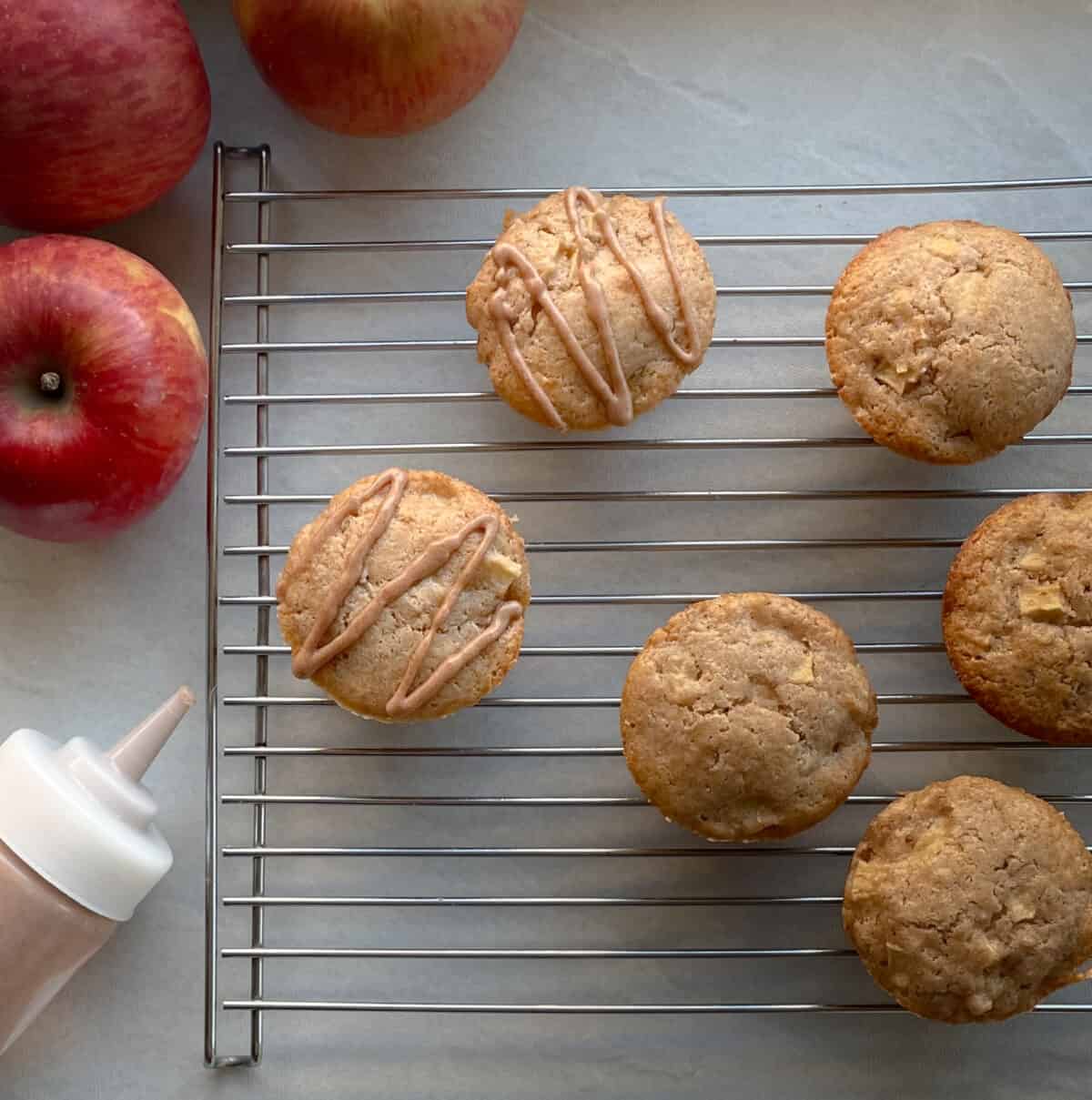 sourdough apple muffins on a cooling rack with glaze and fresh apples.