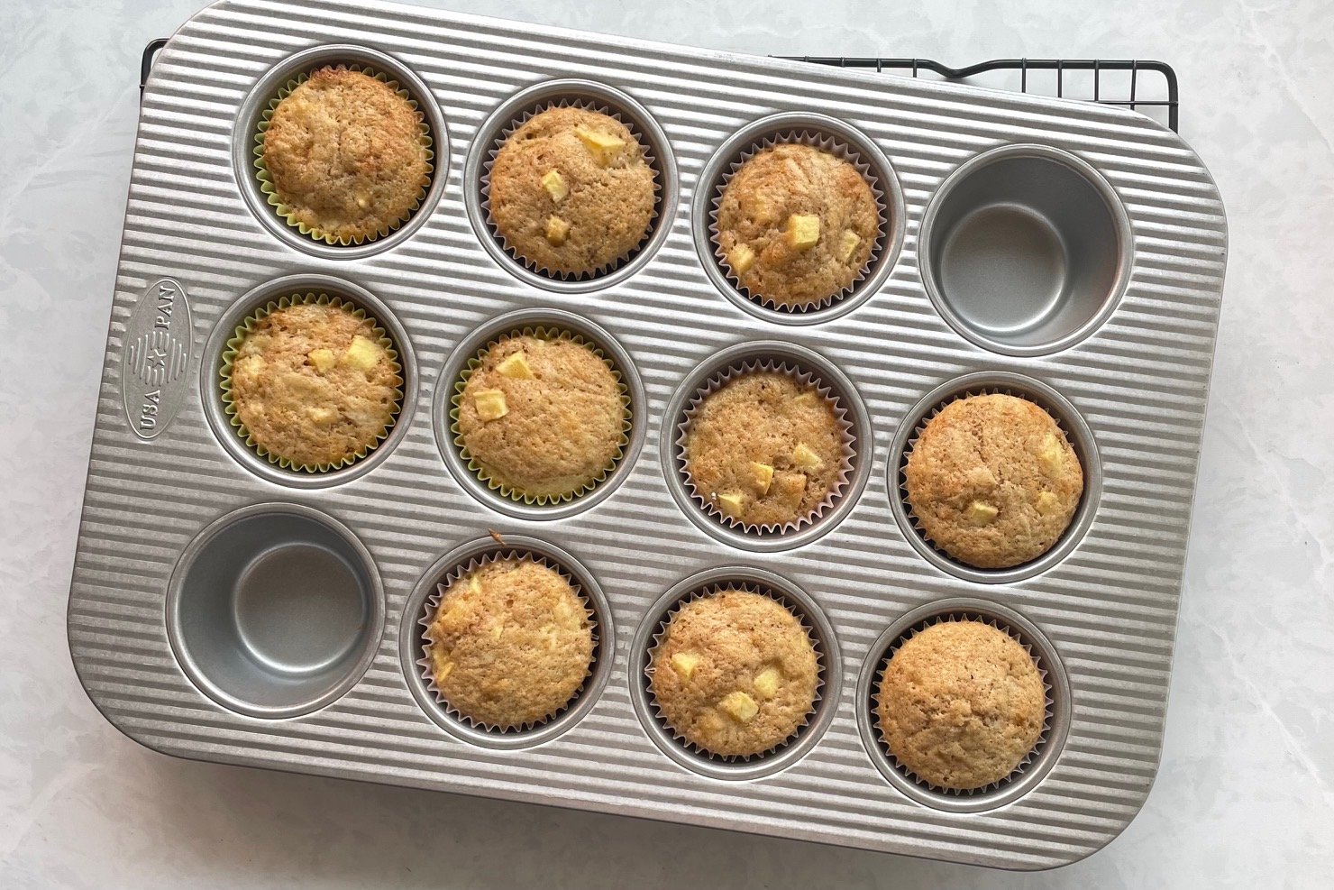 ten baked sourdough apple muffins in a muffin tin on a cooling rack.
