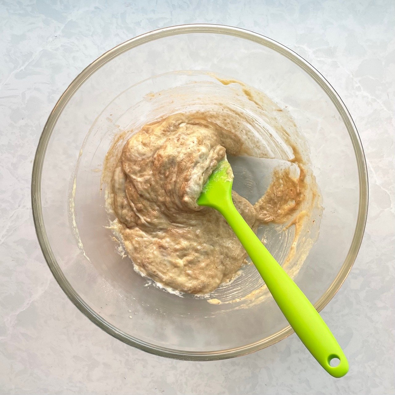 light brown batter with a green silicone spatula in a large glass bowl.
