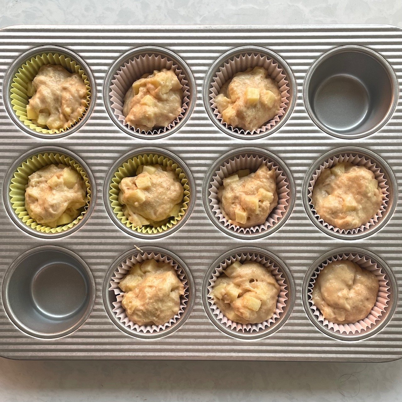 ten muffin tins with apple muffin batter in muffin cups.