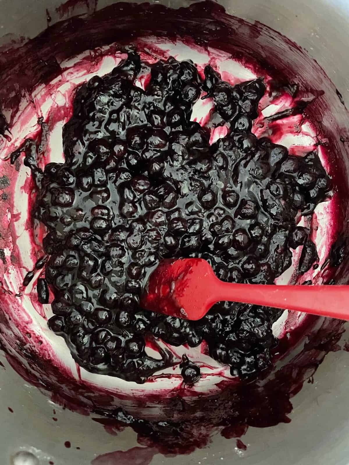 cooked blueberry pie filling in a pot with a red silicone spatula.