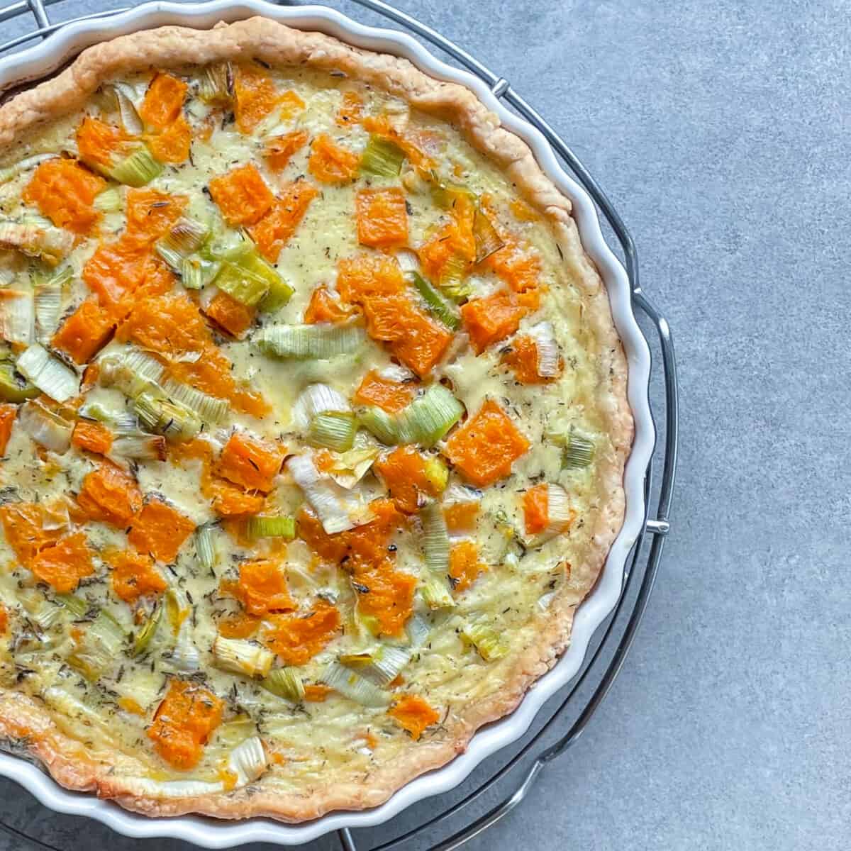 a leek and squash quiche in a blue tart pan.