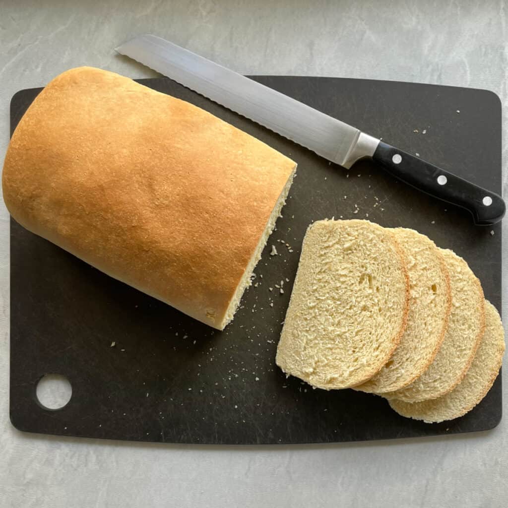 a loaf of semolina bread with four cut slices and  bread knife on a cutting board.