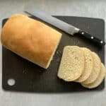 a loaf of yellowish semolina bread, four slices, and a bread knife on a cutting board.