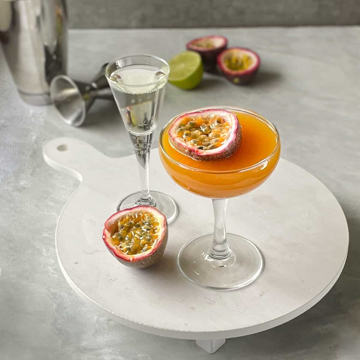 a porn star martini garnished with half a passion fruit on a tray with sparkling wine and passion fruit half.