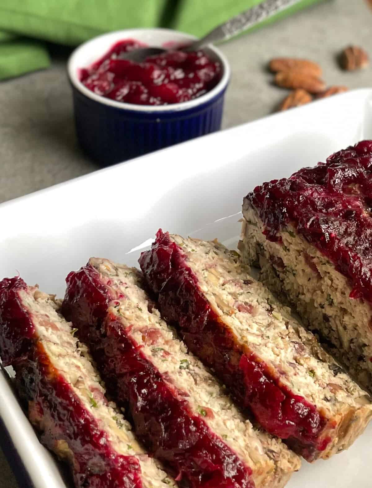 meatloaf glazed with cranberry sauce, a bowl of sauce, and some pecans.