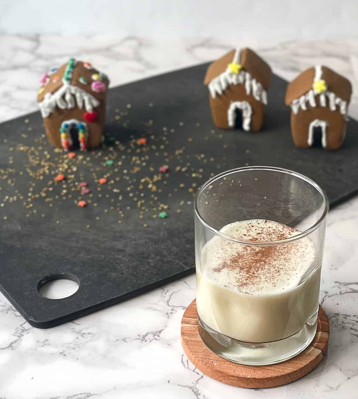 egg nog in a glass in front of three mini gingerbread houses.