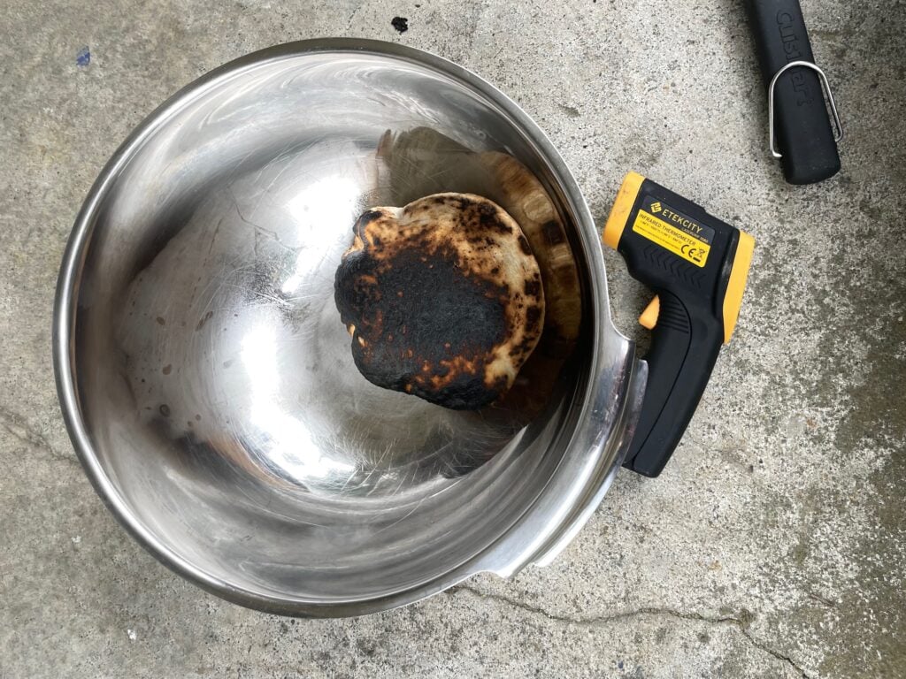 a charred pita in a metal bowl next to a laser thermometer.