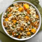 bowl of pumpkin cubes, Israeli couscous, pine nuts, feta, and sprinkled parsley over a green napkin.