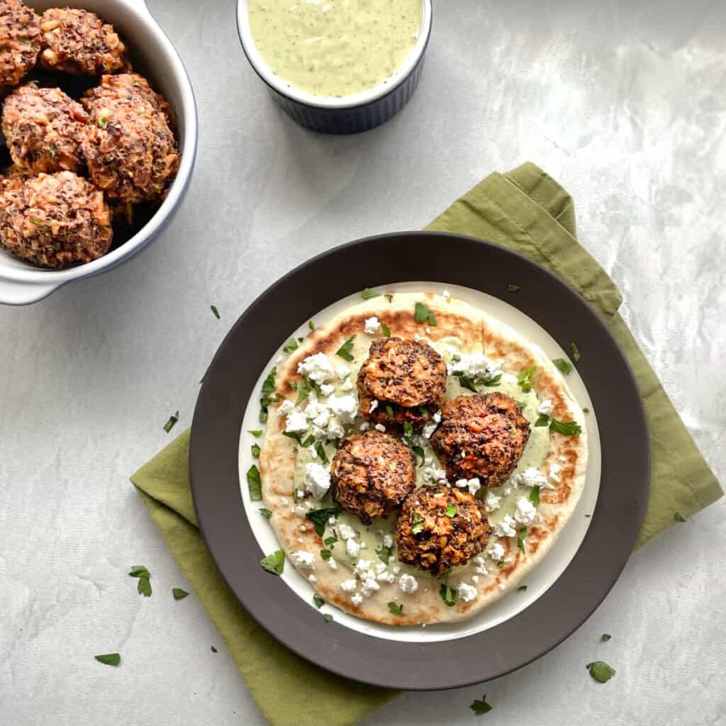 four quinoa balls on a pita with lemon herb tahini sauce, feta, and parsley.