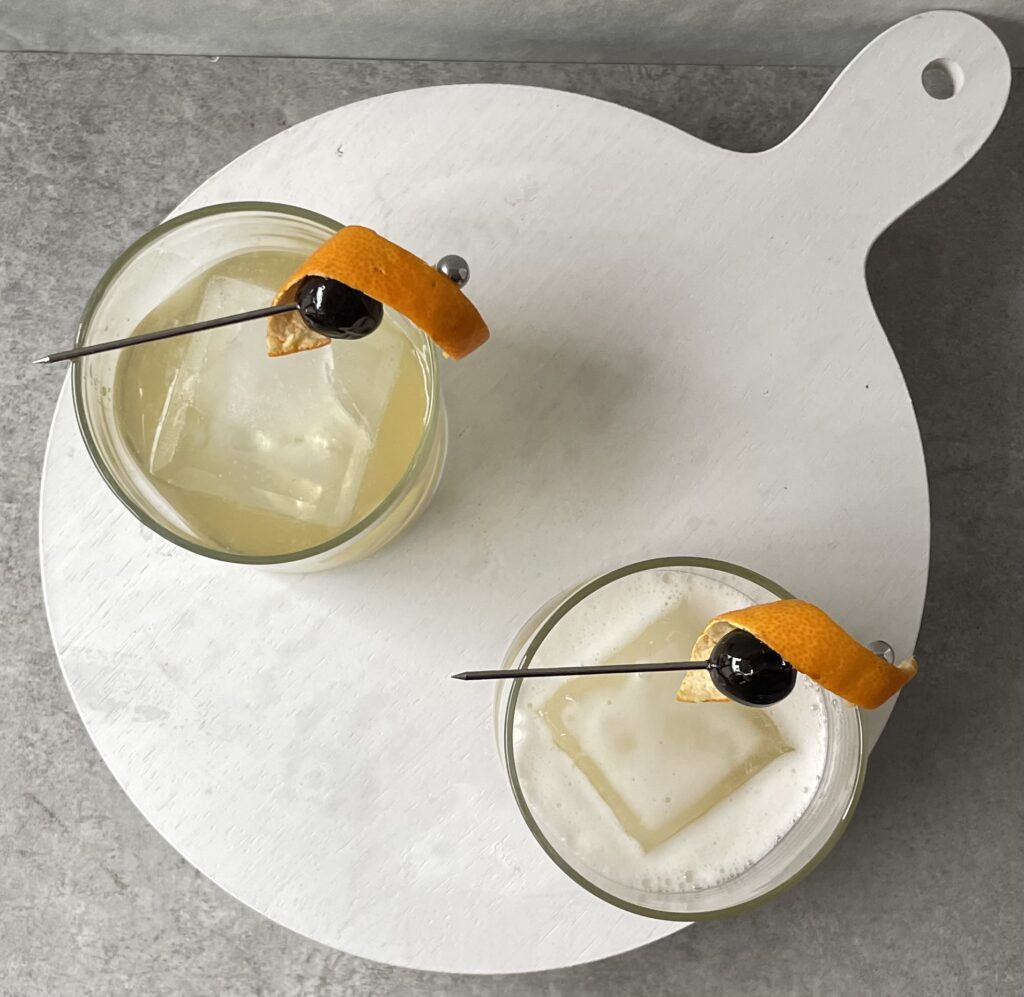 top down photo of two lowball glasses with rock ice, orange twist, and cherry garnish.