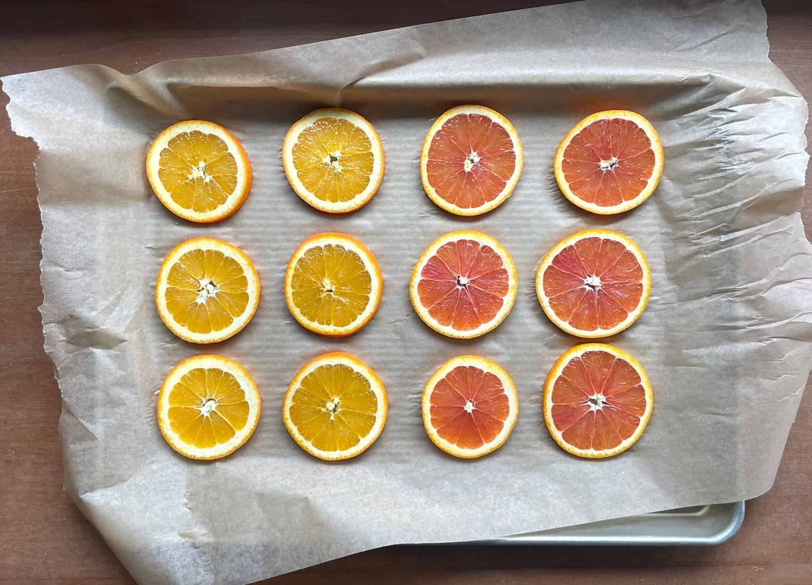 six orange slices and six pink cara cara orange slices on a baking sheet lined with parchment.