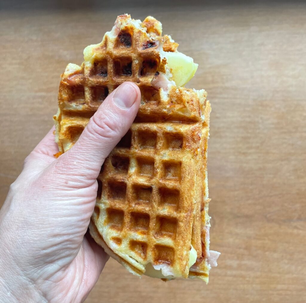 hand holding a ham and cheese waffle cut in half and filled with apple slices.