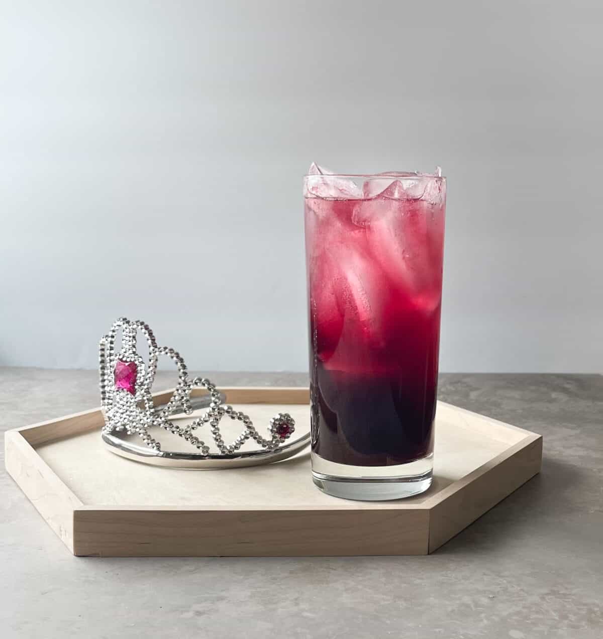 dark pink highball cocktail on a tray with a tiara.