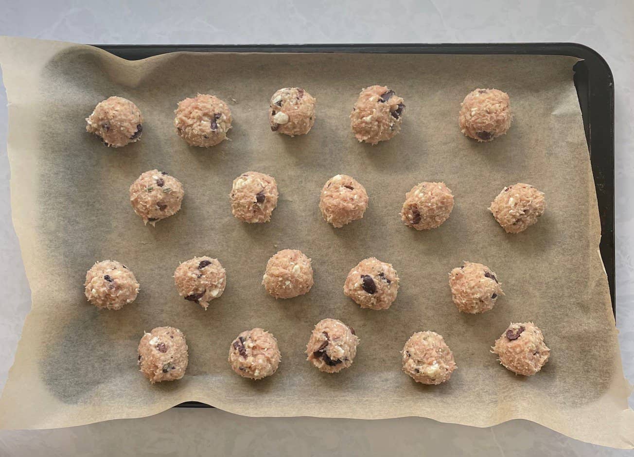 unbaked chicken meatballs with feta and olives on a parchment-lined sheet.