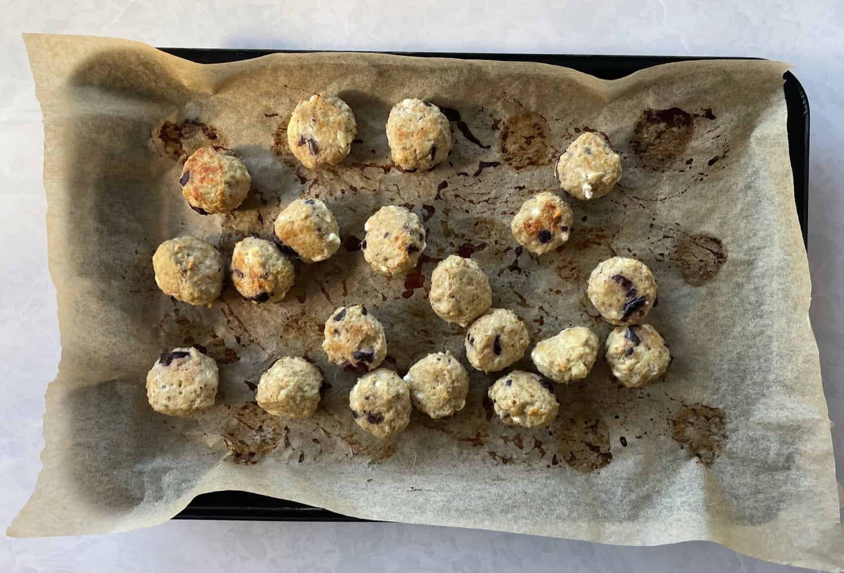 baked chicken meatballs with olives and feta on a parchment-lined sheet.