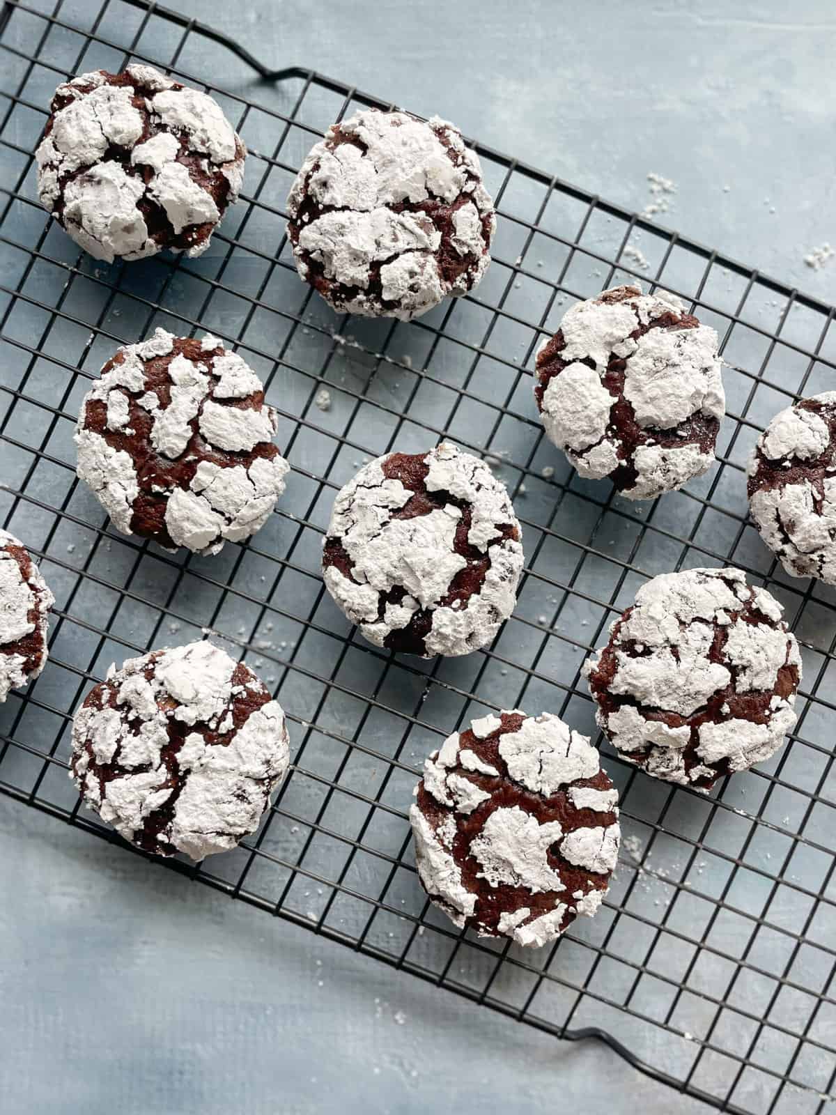 baked chocolate crinkle cookies on a baking rack with powdered sugar everywhere.