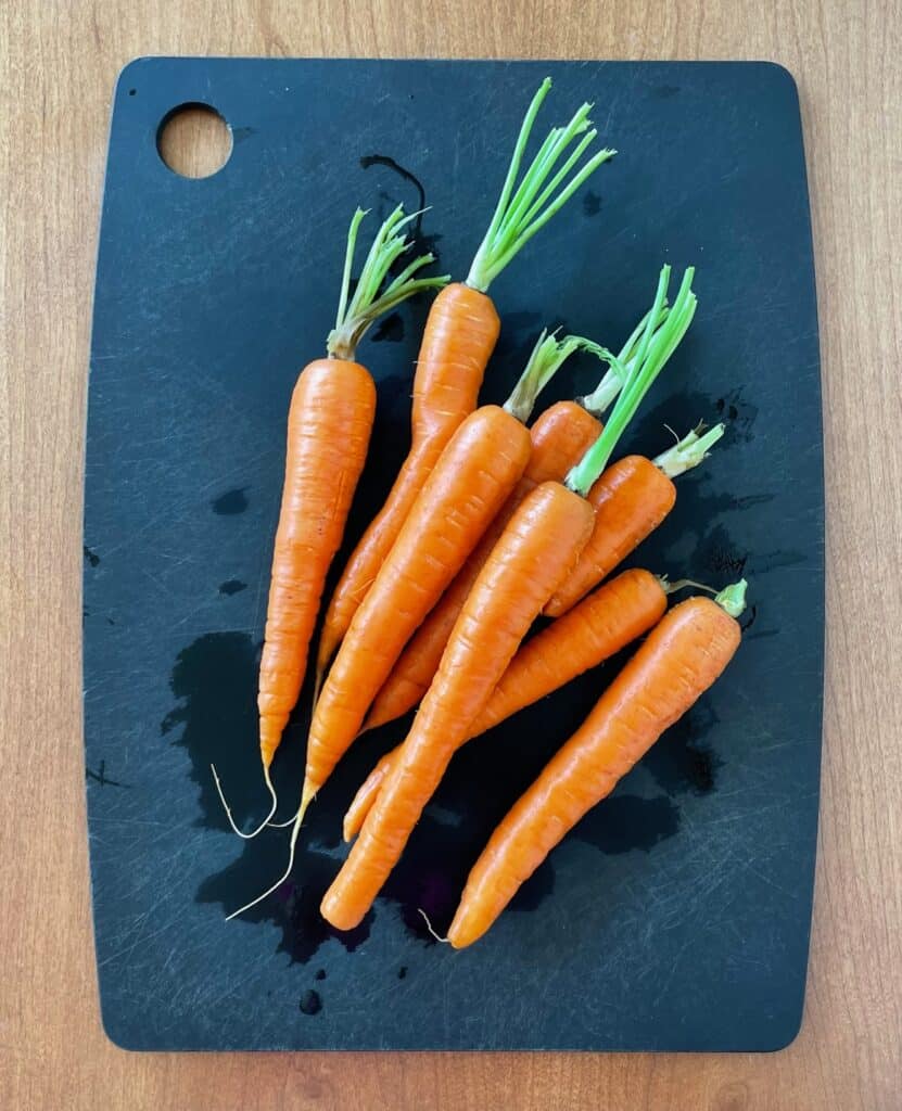 eight orange carrots with trimmed stems on a black cutting board.