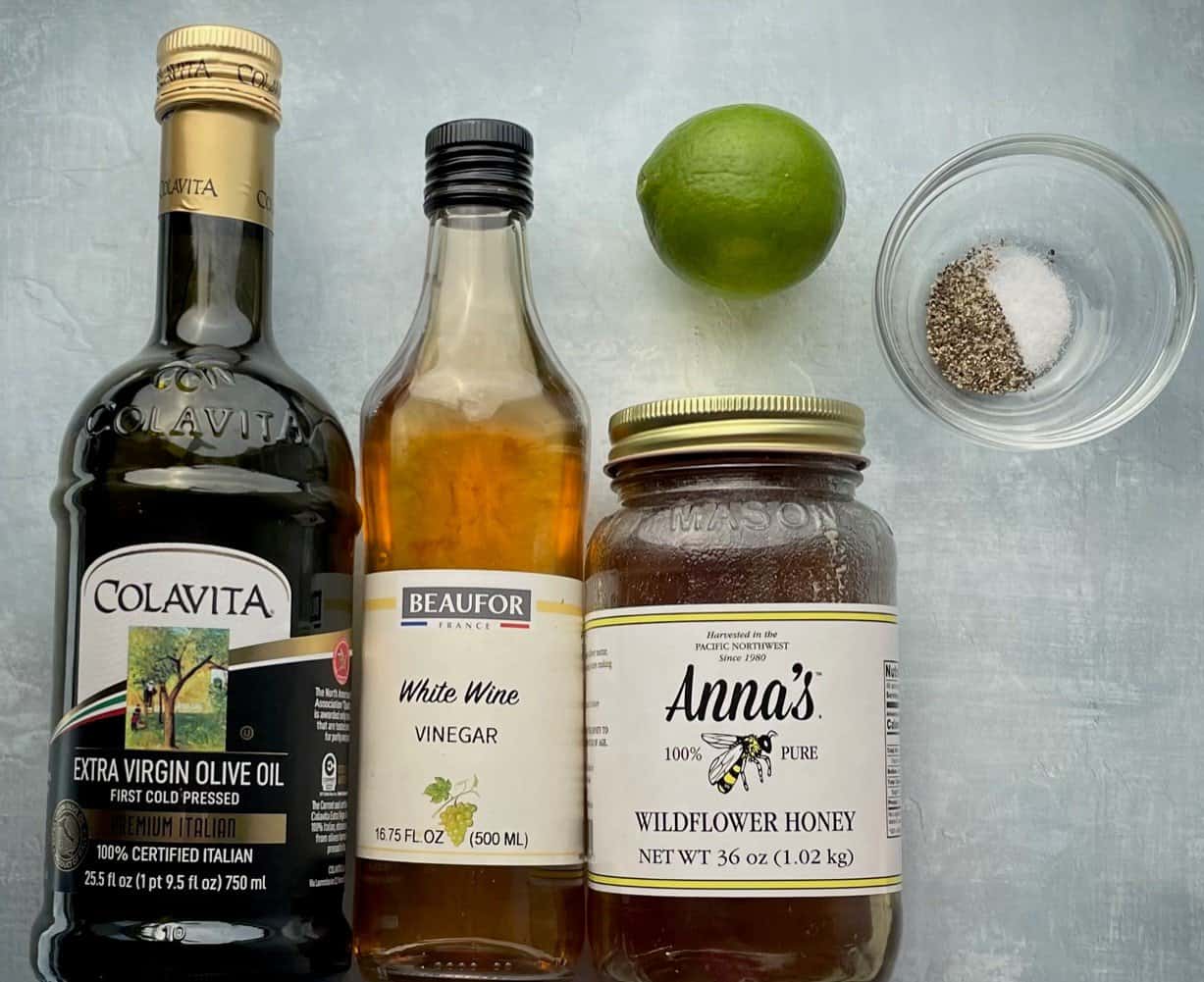 extra virgin olive oil, white wine vinegar, honey, lime, and small bowl of salt and pepper on a countertop.