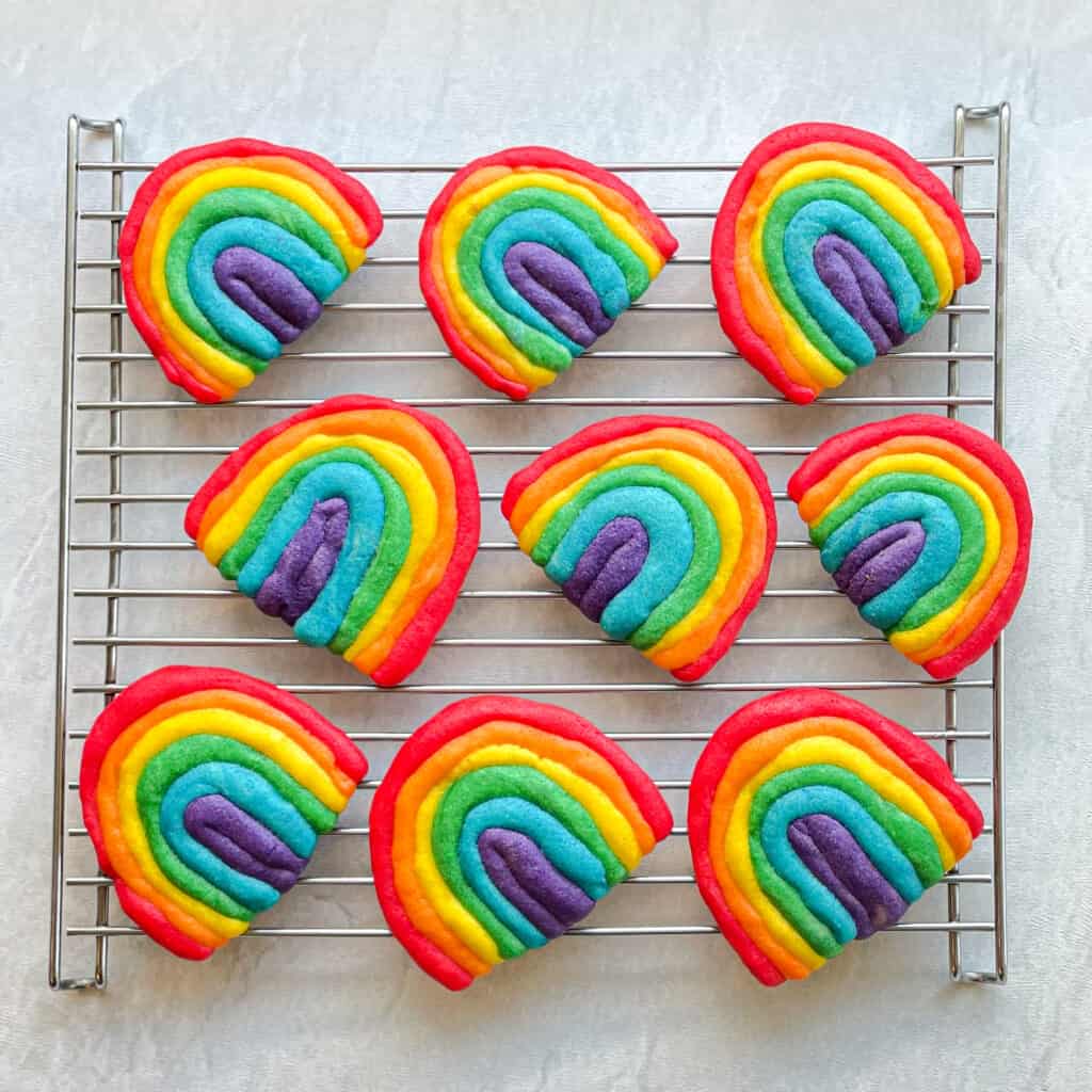 rainbow colored sugar cookies shaped like rainbows on a cooling rack.