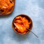 fork and small bowl of strips of raw carrot salad with a larger bowl of carrots in the corner.