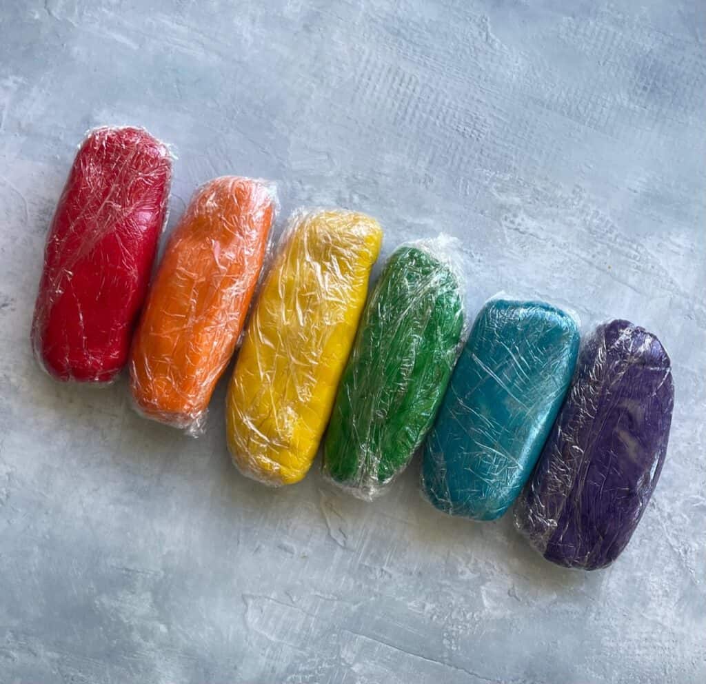 six rainbow colored cookie doughs wrapped in plastic.