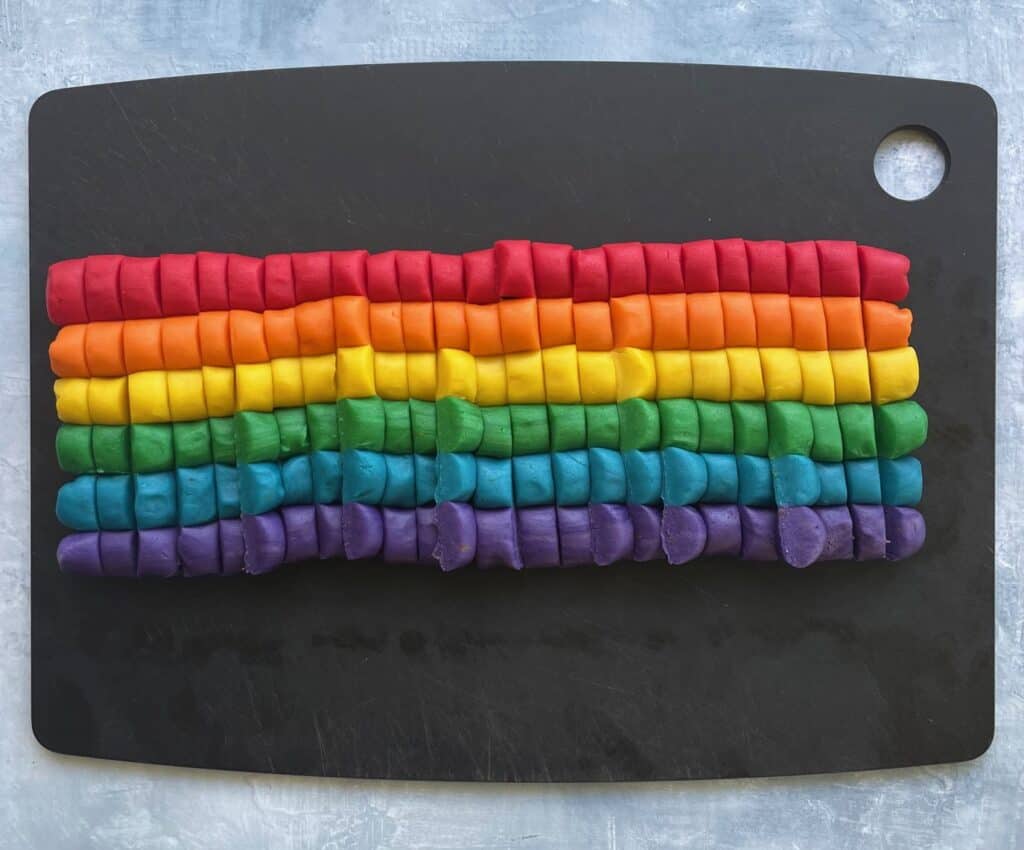 logs of rainbow colored cookie dough cut into many small pieces on a cutting board.
