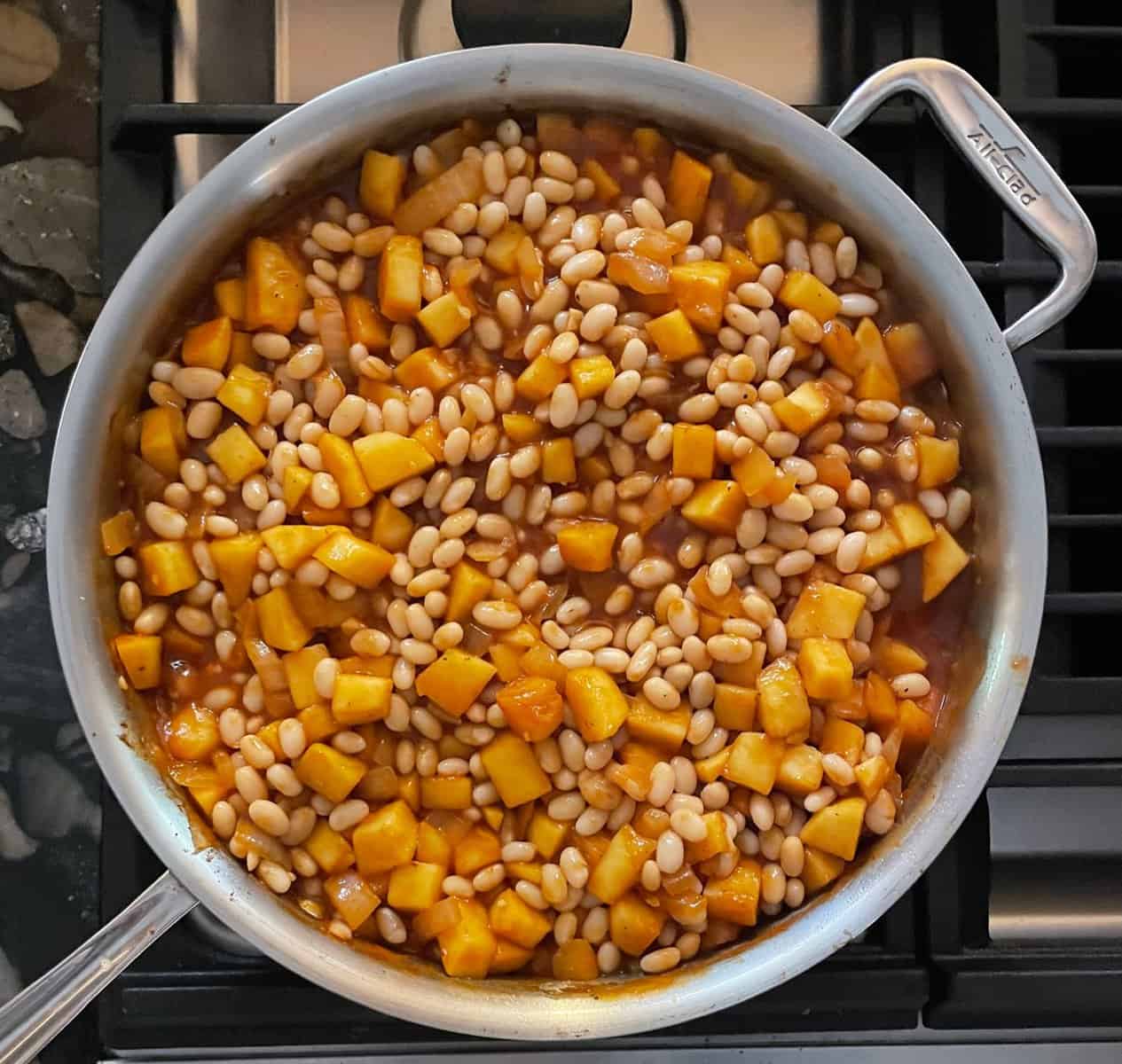 pan on the stove top with beans and apples and bbq sauce.