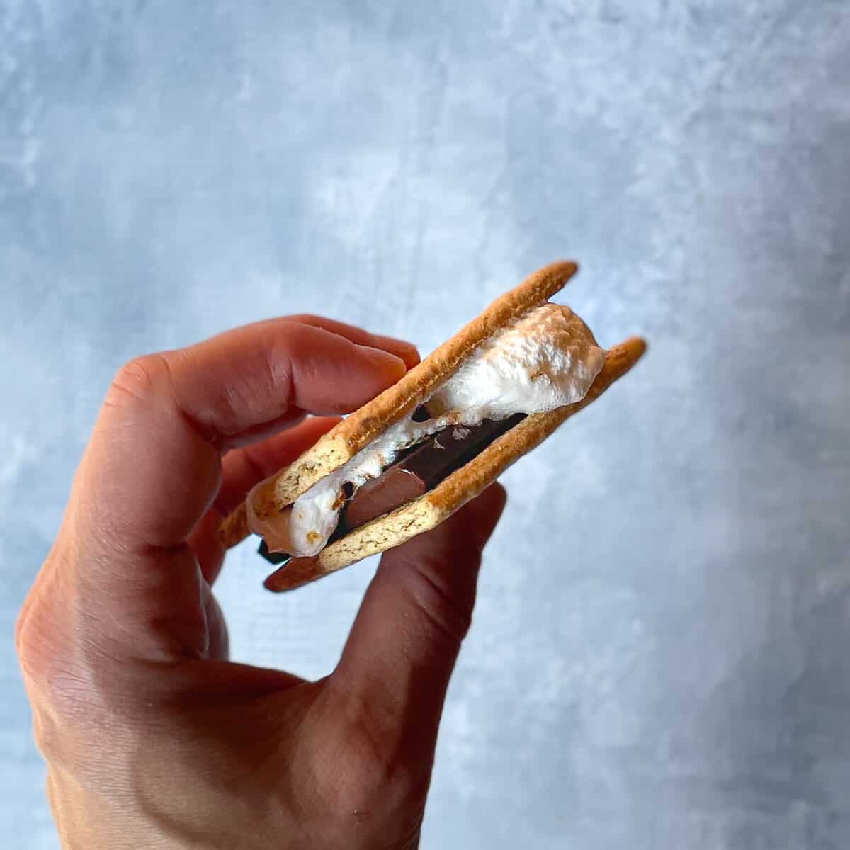 hand holding a smore with oozing marshmallow, melted chocolate, and graham crackers.