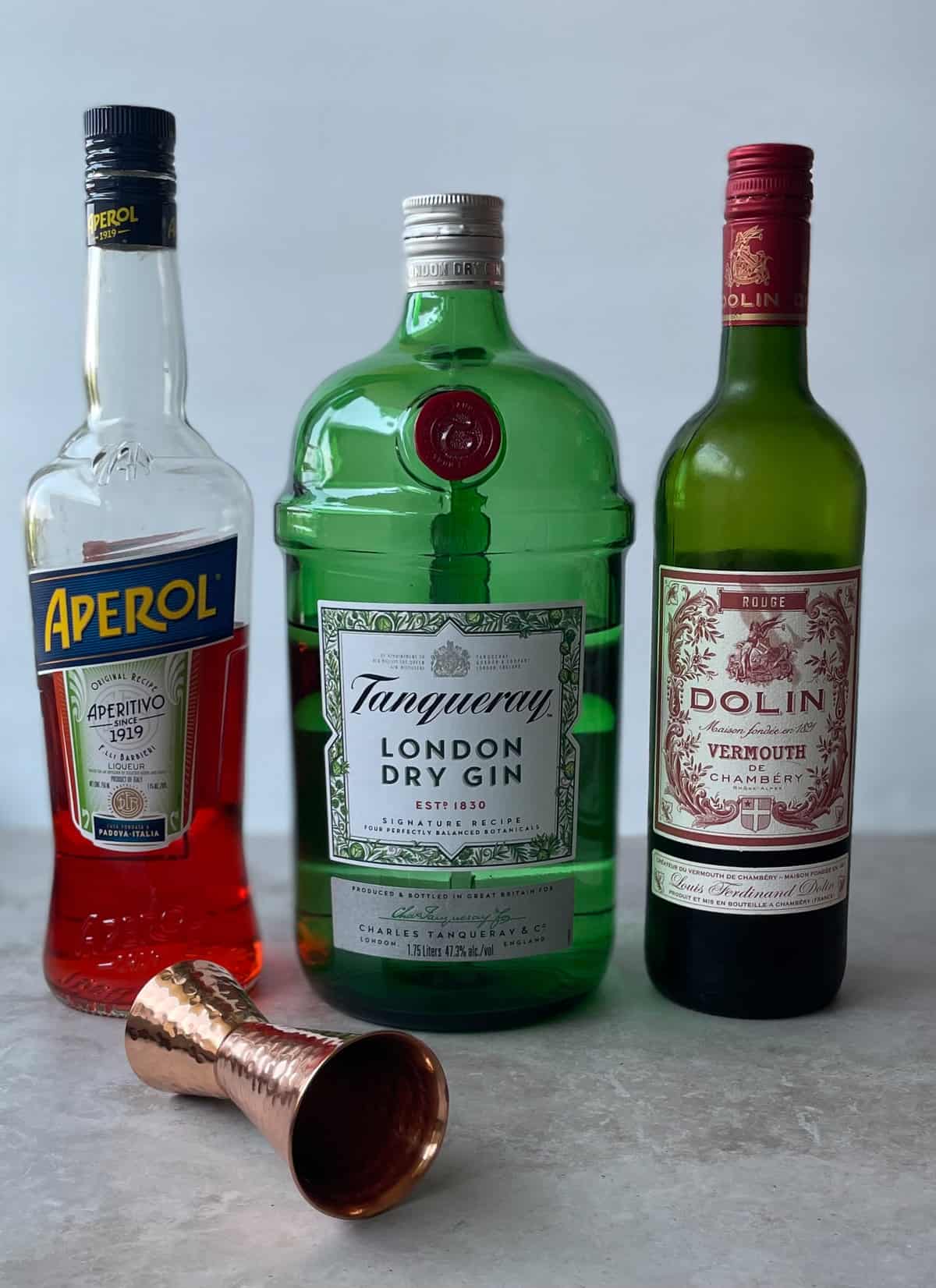 bottles of Aperol, gin, sweet vermouth, and a jigger on a countertop.